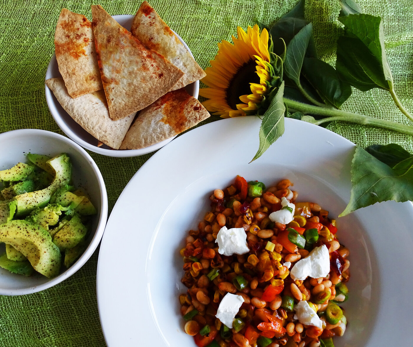 A bright fresh medley of dishes: Charred corn salad, zingy avocado and crispy tortillas are presented next to a sunflower