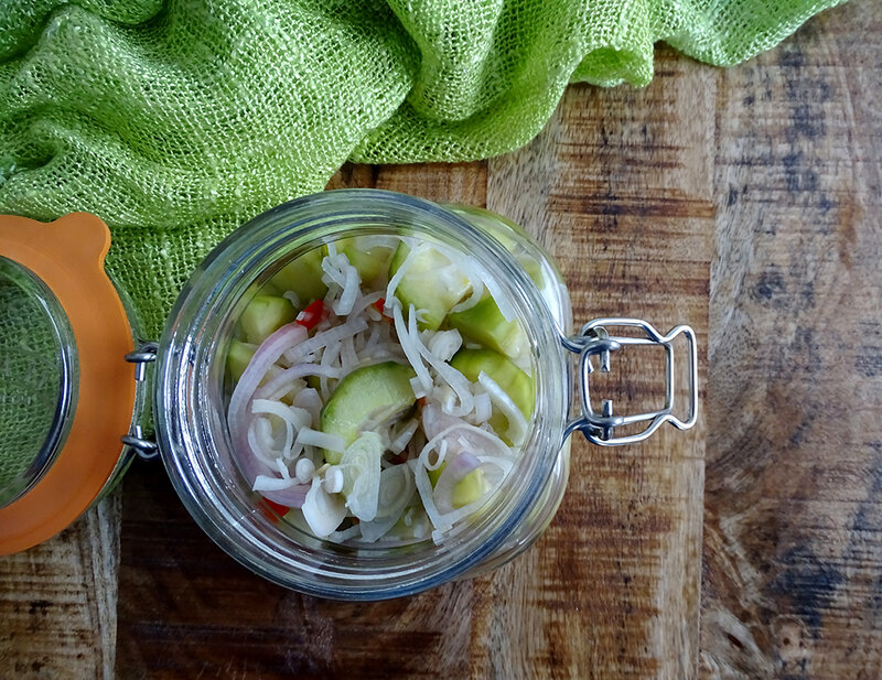 The pickle is in a jar. The brilliant green of the cucumber is mirrored by a green tablecloth