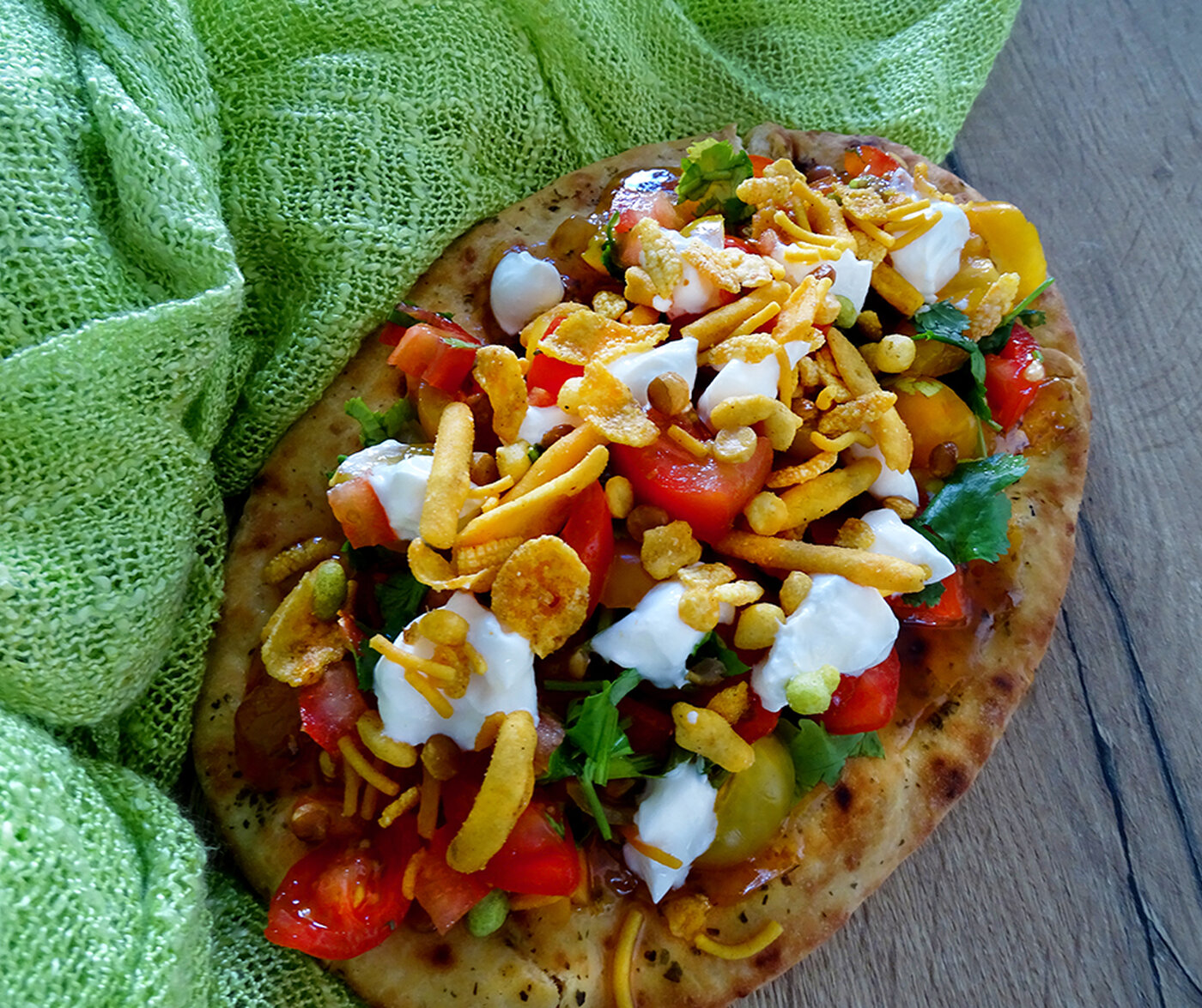 The naan is topped with an explosion of colour - red tomatoes, green coriander. orange chutney, and little dollops of white creme fraiche